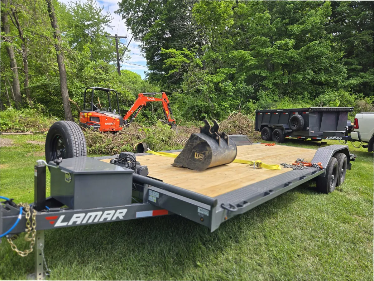 Mini-excavator and bucket loaded on the open-deck car hauler for a land-clearing job