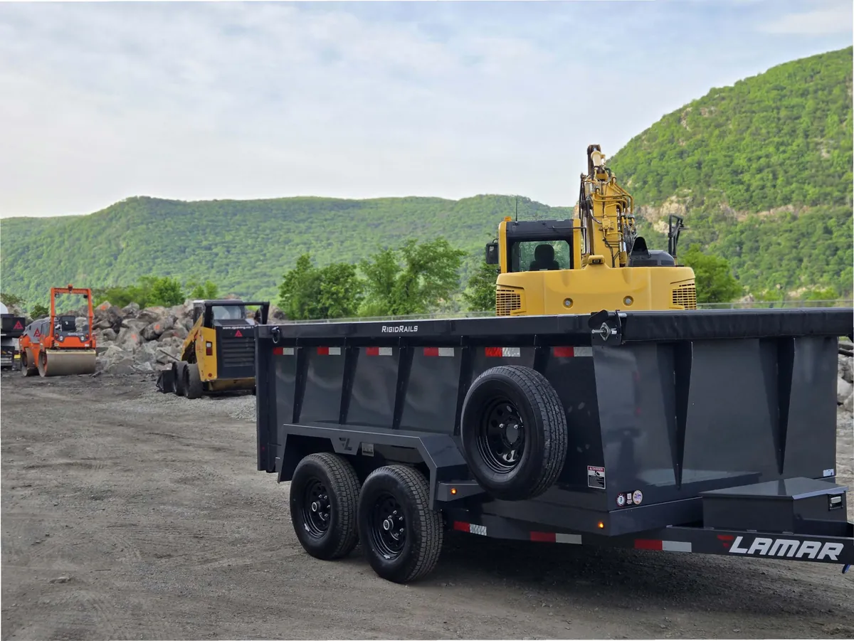 Mainline dump trailer loaded out at a quarry with an excavator and mountains behind